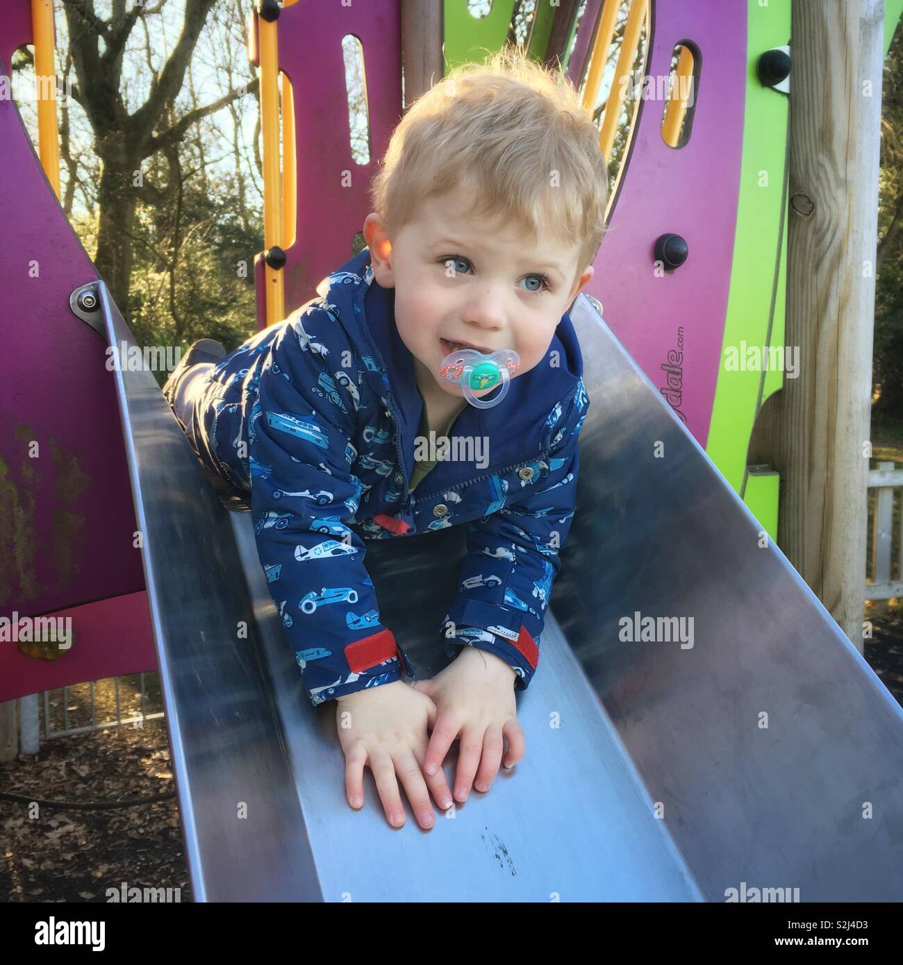 Two year old boy on a metal slide, Medstead, Alton, Hampshire, England,United Kingdom. - Smartphone Captured Stock Image