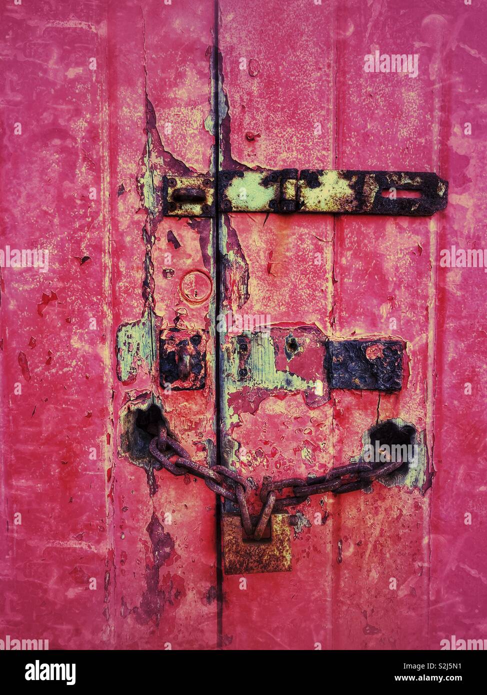 Old fading red garage door with rusted locks. - Smartphone Captured Stock Image