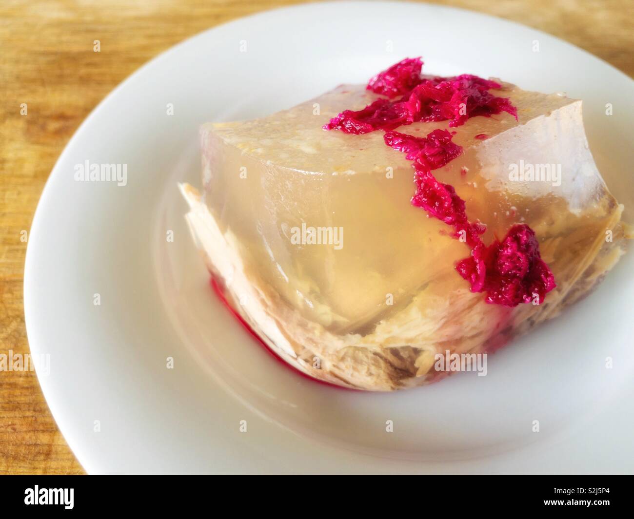 Big plate with Ukrainian aspic flavored with horse-radish pickled in beetroot juice standing on wooden surface Stock Photo