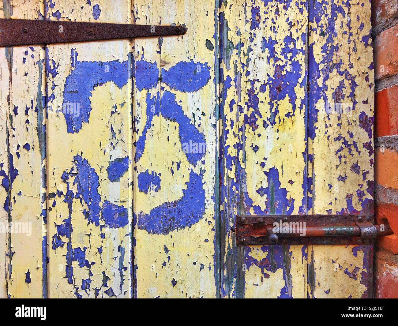 Old outside toilet door with flaking pale yellow paint revealing old purple paint beneath. - Smartphone Captured Stock Image