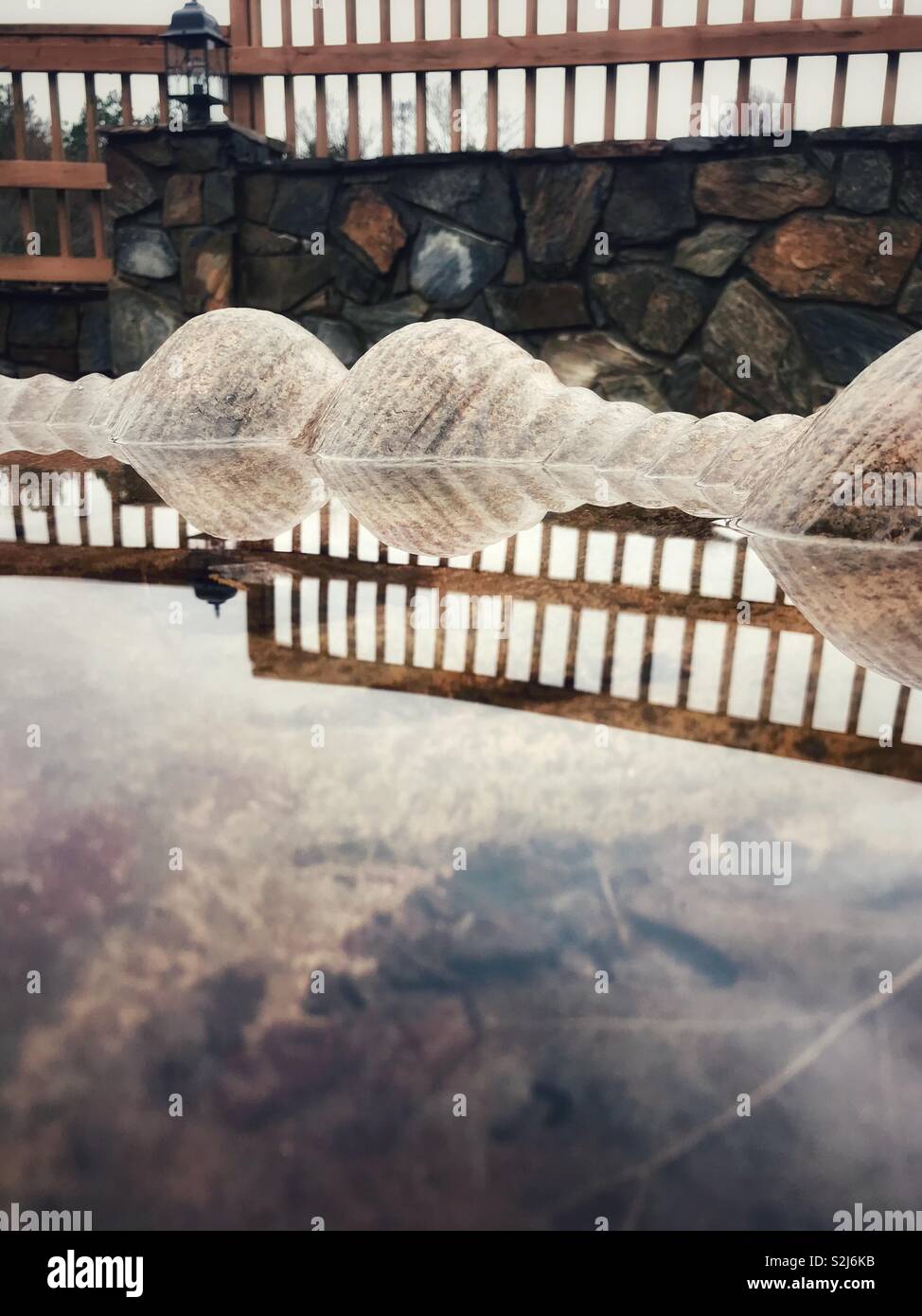 Fence line on stone retaining wall and clouds reflected in fountain water - Smartphone Captured Stock Image