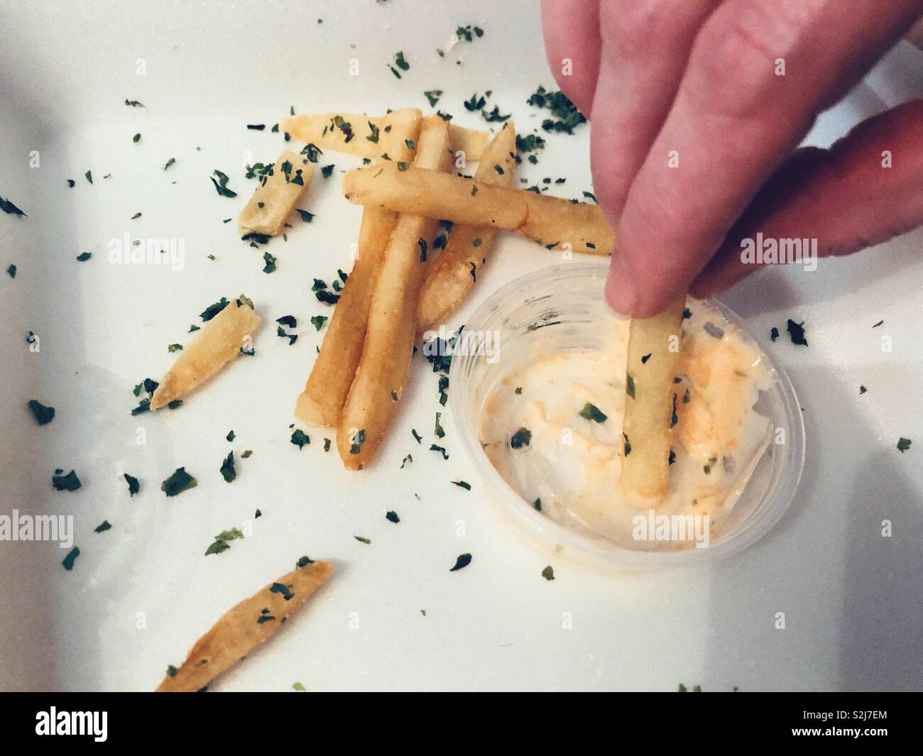 Close up of hand dipping French fry sprinkled with sea weed with a Japanese Mintai Mayo in a plastic cup, in a takeout styrofoam box Stock Photo