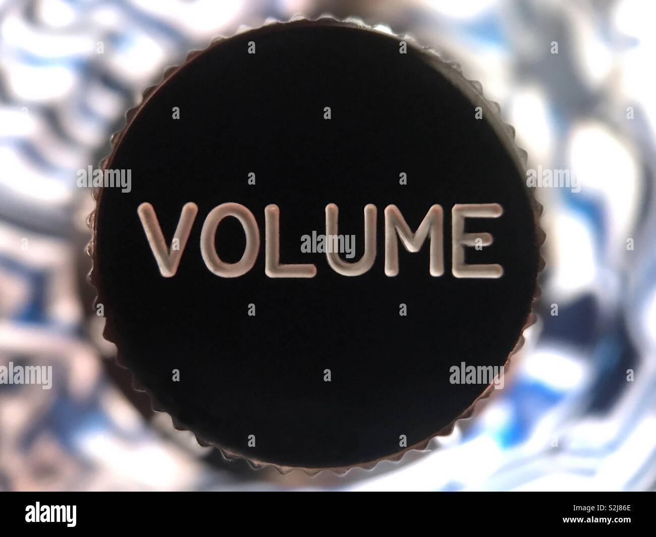 A black, plastic, electric guitar knob, with VOLUME imprinted in white, is shown in a macro closeup view. - Smartphone Captured Stock Image