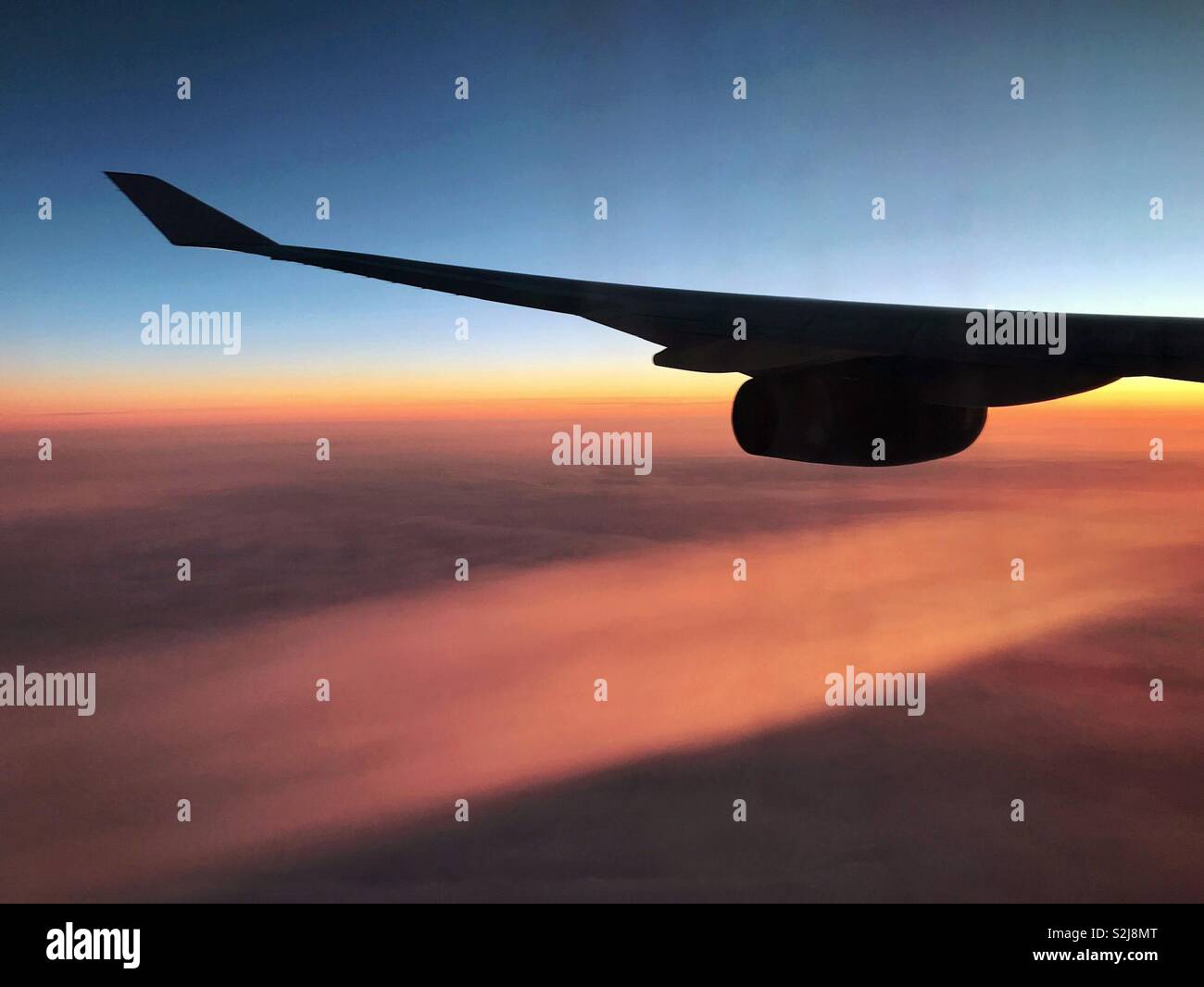 Silhouette of a jet’s wing with contrail from engine at sunset - Smartphone Captured Stock Image