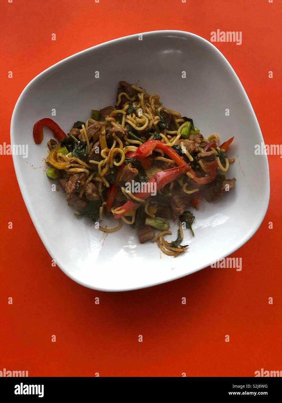 Stir fry beef in a white square bowl sat on an orange background. Stock Photo