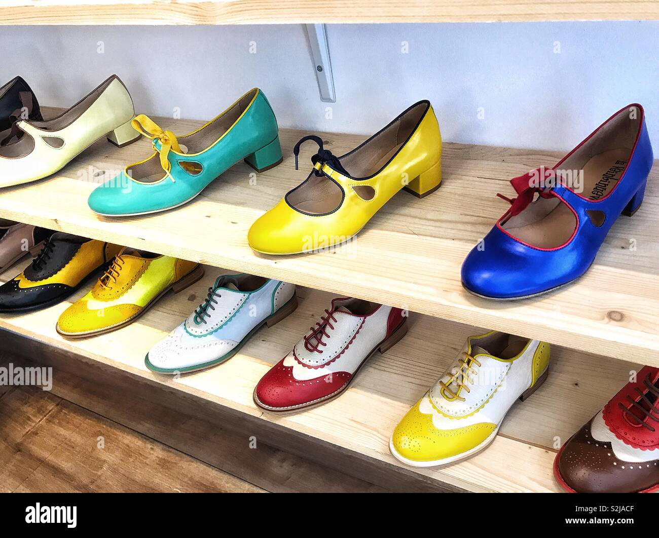 A display of designer shoes in a range of bright colours, arranged on  wooden shelving in a shoe shop Stock Photo - Alamy