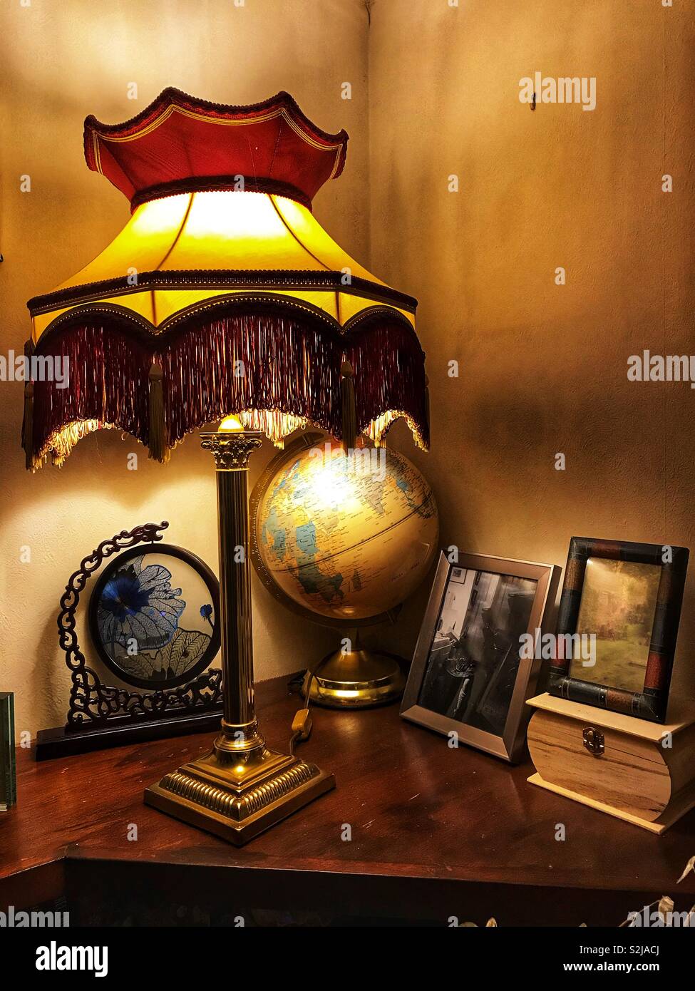 A lamp, family photos and a globe on a ledge in a corner of a room. - Smartphone Captured Stock Image