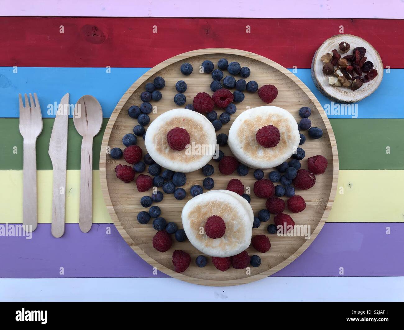 Pancake with blueberries, raspberry and dry fruit on a multi colored wooden board and wood cutlery Stock Photo