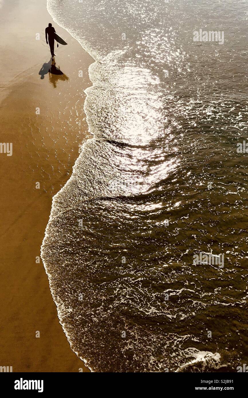 Surfer walks down the beach. Manhattan Beach, California USA. Stock Photo