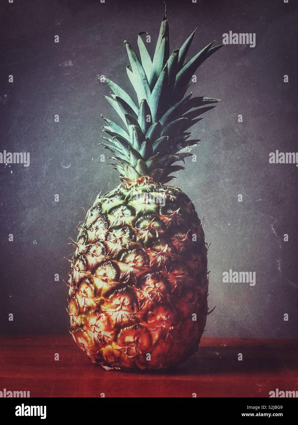 Pineapple on wooden surface with grey background Stock Photo