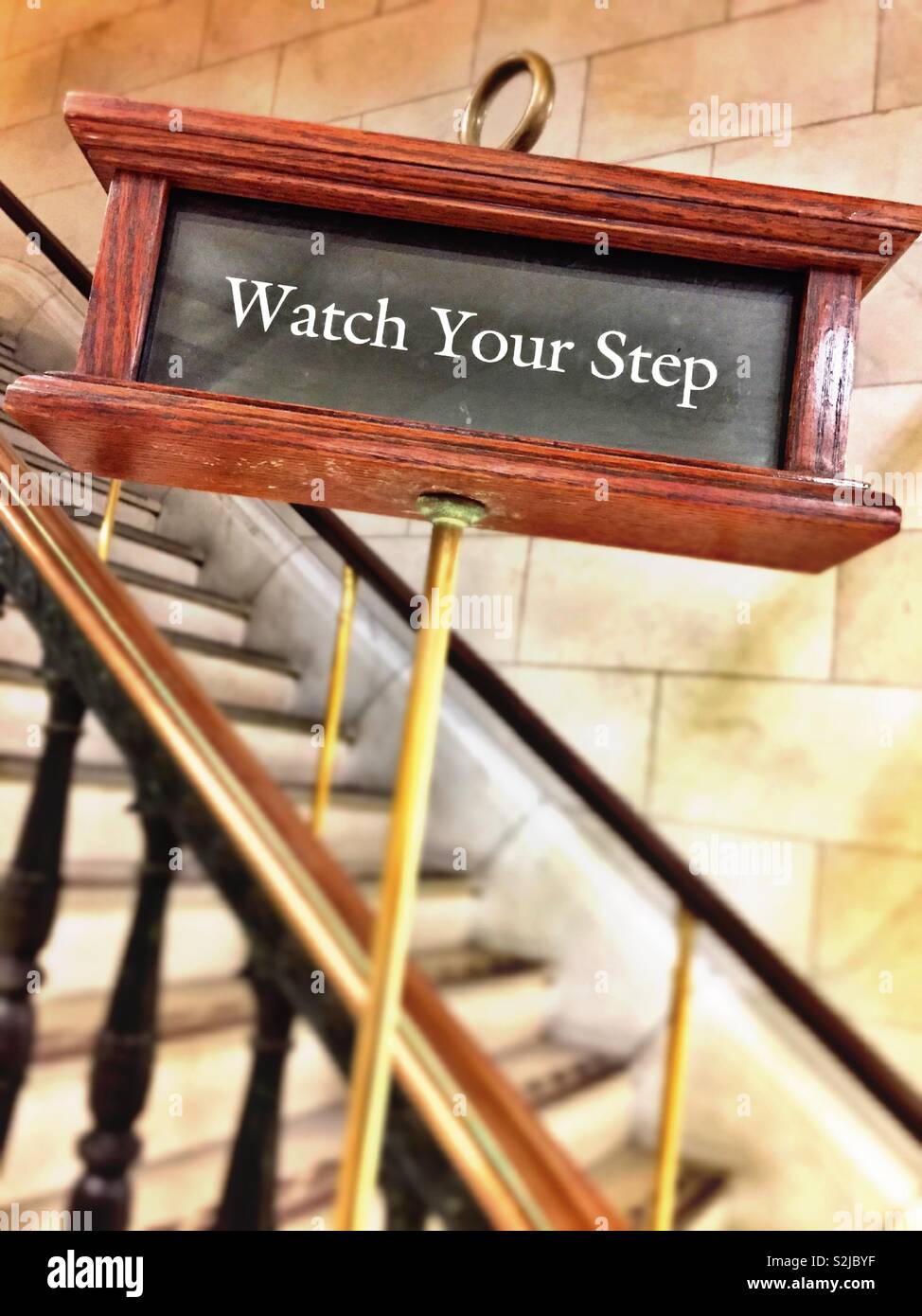 Elegant wooden and brass watch your step warning sign on a flight of interior stairs, USA Stock Photo