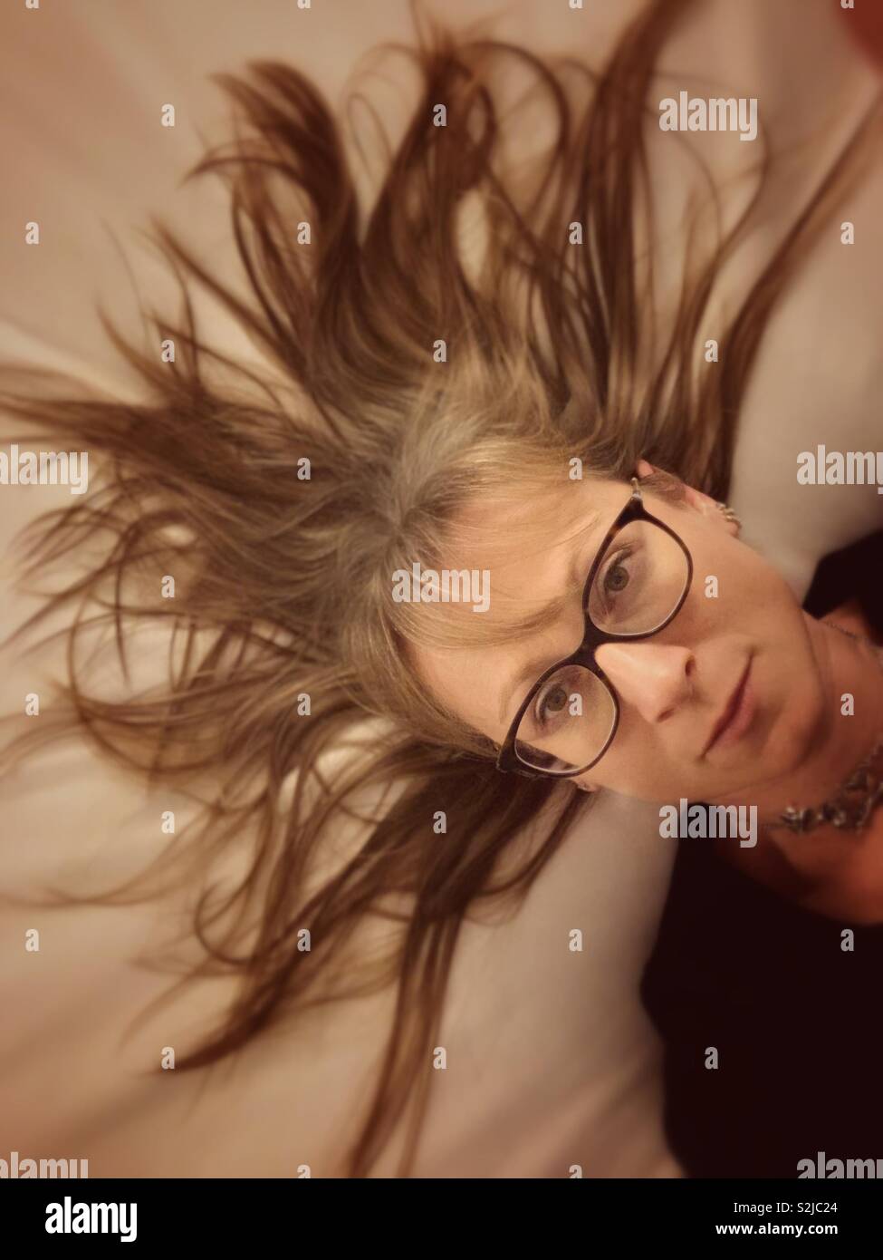 Selfie of a woman lying in bed with hair spread around like a crown. - Smartphone Captured Stock Image
