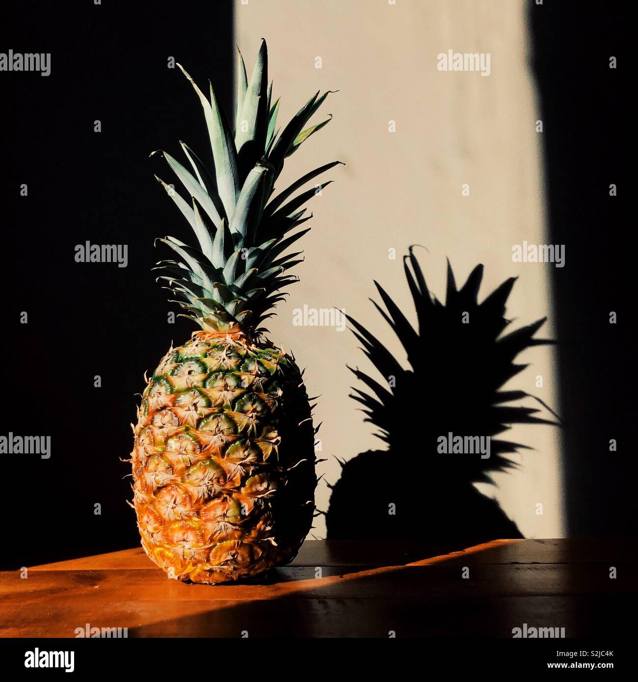 Pineapple on wooden surface in beam of sunlight creating shadow - Smartphone Captured Stock Image