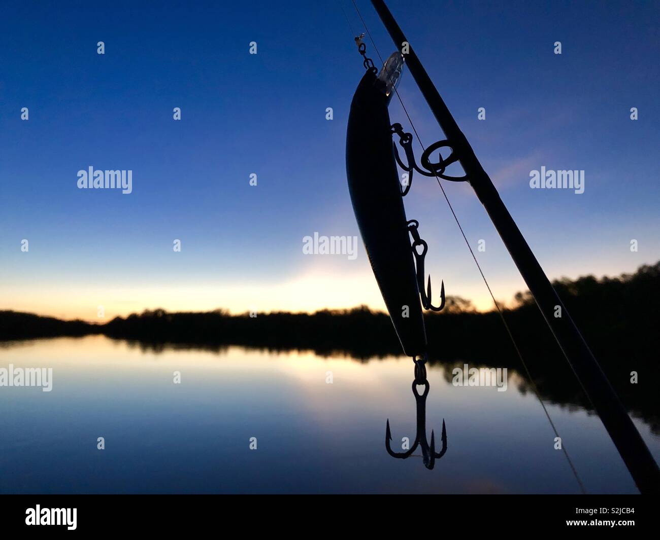 Silhouette of a fishing lure and fishing rod against a sunrise over Tommy Cut Creek in the Northern Territory of Australia. - Smartphone Captured Stock Image