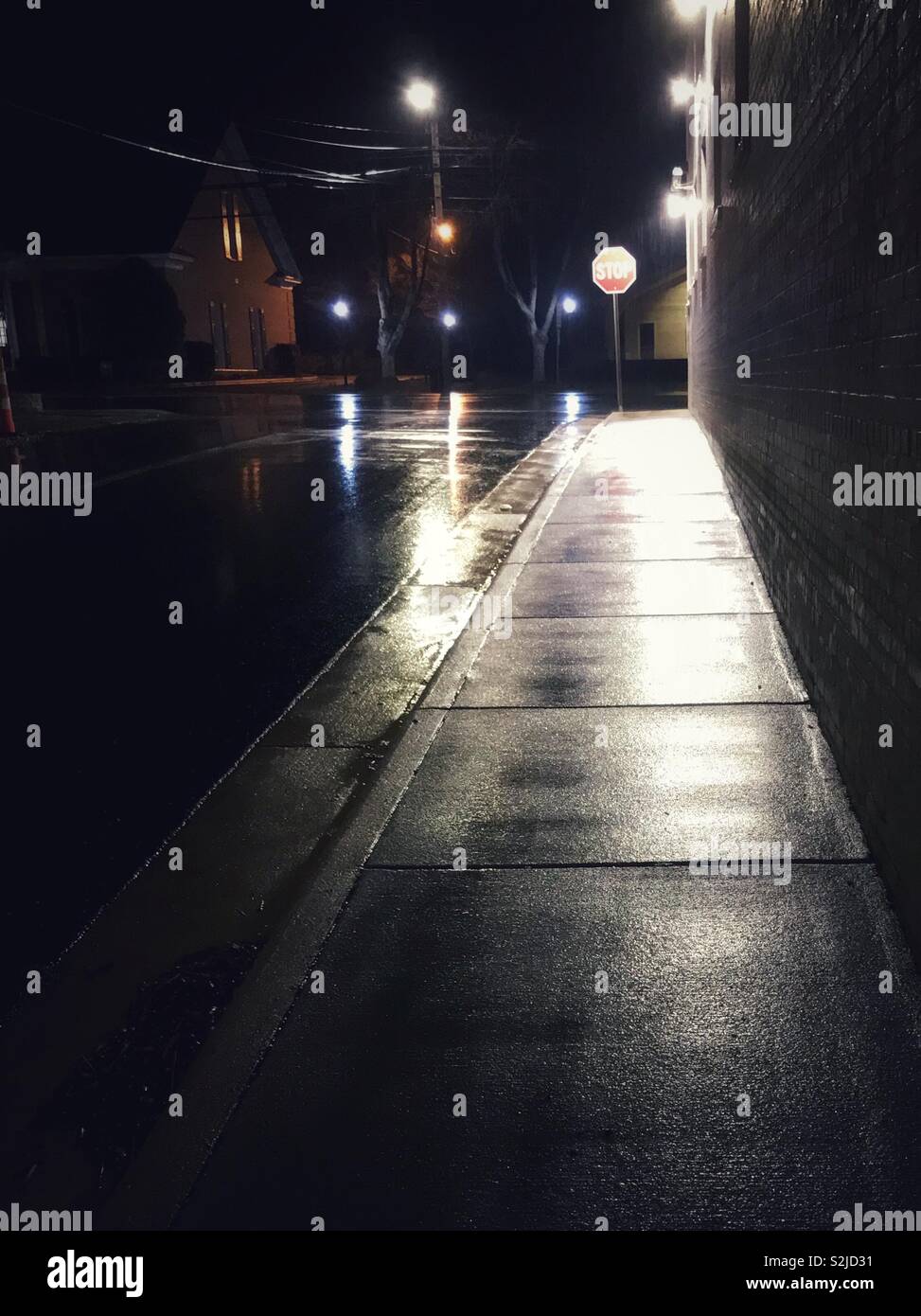 Rain soaked sidewalk reflects streetlight after dark - Smartphone Captured Stock Image
