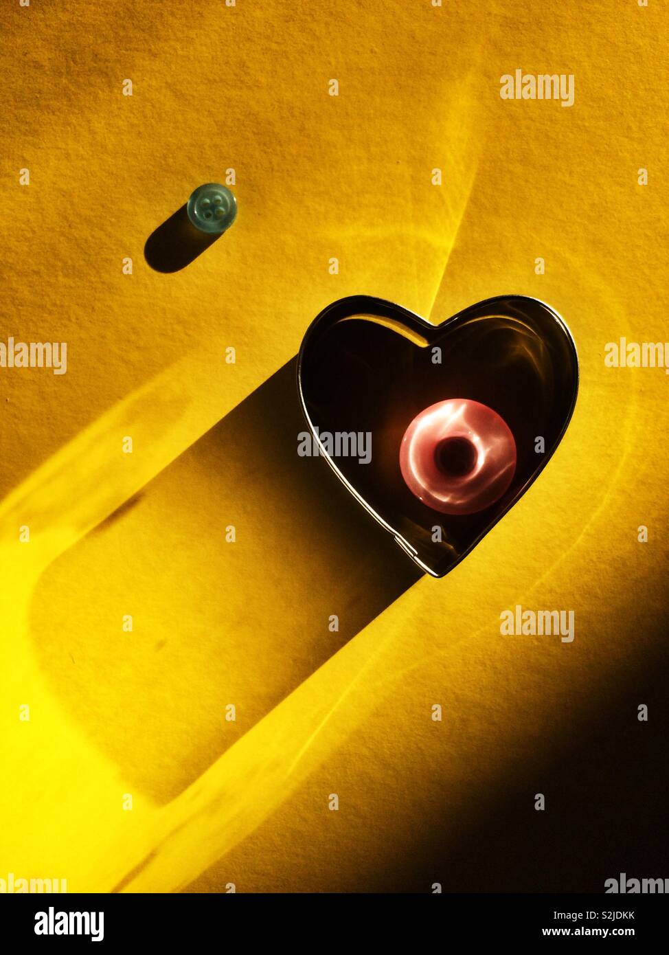 Metallic heart and buttons on yellow background - Smartphone Captured Stock Image