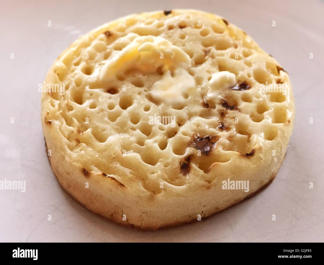 Hot buttered crumpet.  Lovely English breakfast food.  Buttery melting into the tiny baked holes.  Delicious start to the day and served with a cup or pot of tea.  Toast or toasted Stock Photo