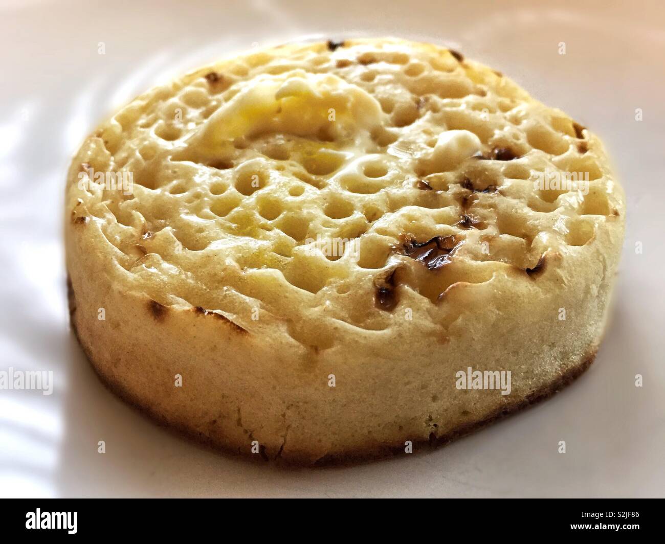 Hot toasted and buttered crumpet.  Food for the morning and great for breakfast.  Served with coffee or tea.  Cooked and eat with jam or marmalade Stock Photo