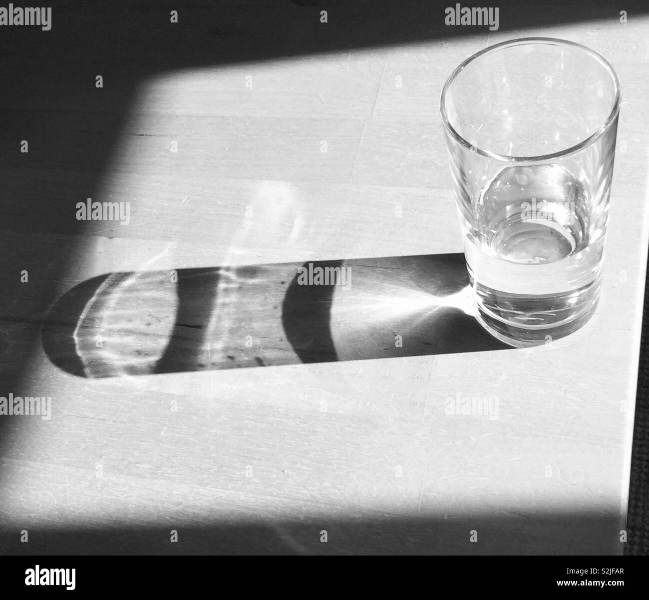 Glass of water with sunlight reflecting through and creating patterns - Smartphone Captured Stock Image