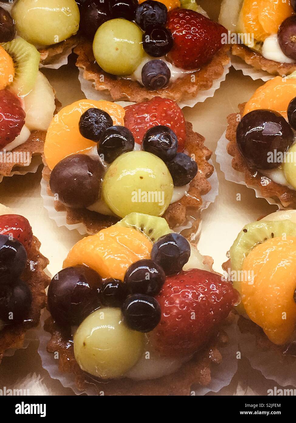 Mouth watering delicious tasty treats professionally prepared fruit tarts including blueberries, kiwi, purple and green grapes, orange, and strawberries. Stock Photo