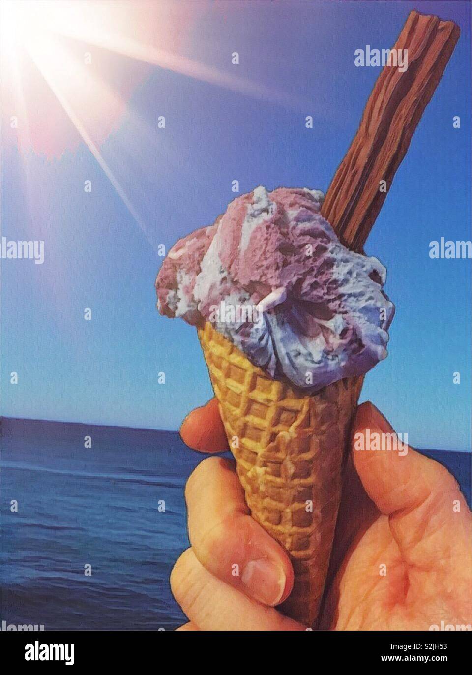 Ice cream in the hot summer sun by the seaside.  Sun and rainbow bubblegum blue purple ice cream in a cone with a chocolate. Lick tongue and taste sugary food - Smartphone Captured Stock Image