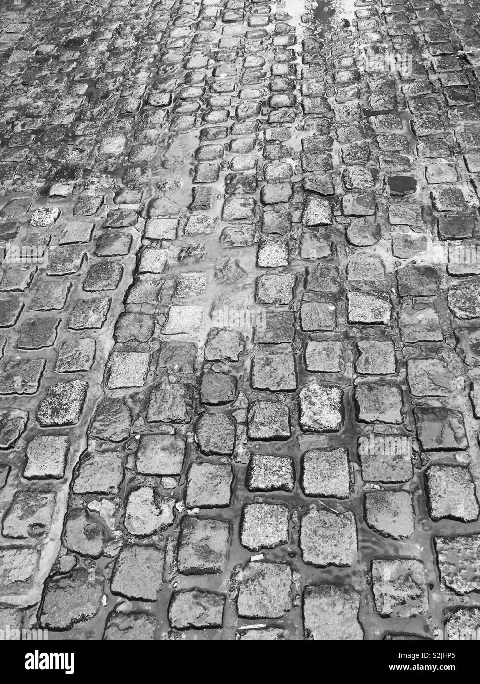 Wet and damp cobblestones on a rainy day.  Rain pouring down on the roads and streets of the ground. Cobbles soaked with rain.  Murky weather.  Cobbled Lane Stock Photo