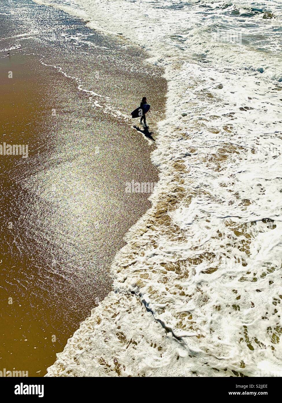 Surfer walks down the beach. Manhattan Beach, California USA. Stock Photo