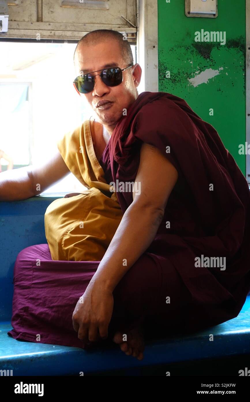 Cool monk! Portrait of a Burmese buddhist monk wearing sunglases. Photographed in a moving train at the open window with bright sunlight. In Yangon, Myanmar. Stock Photo