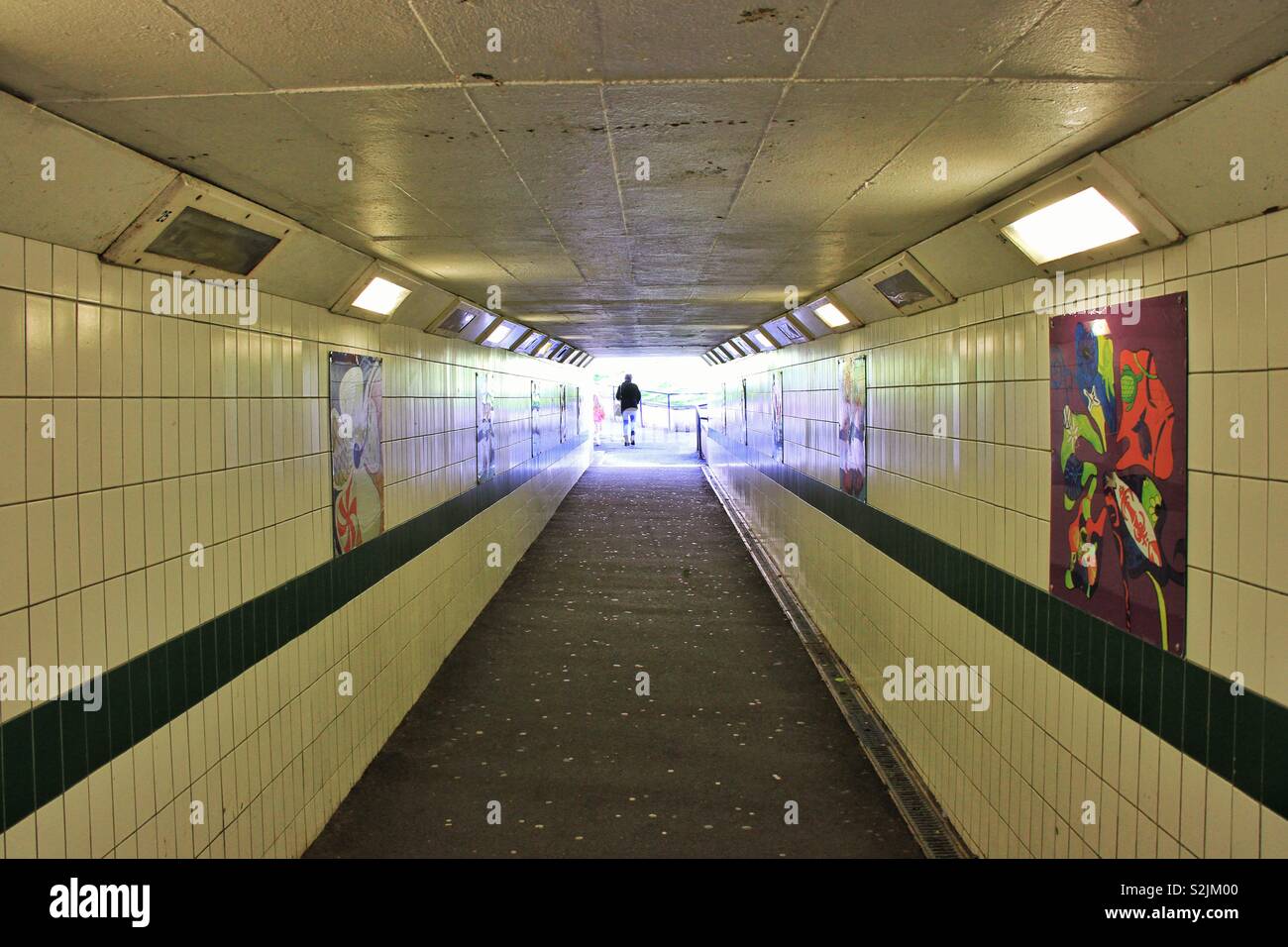 Solitary figure in subway basked in multicoloured light with artwork on display on tiled walls Stock Photo