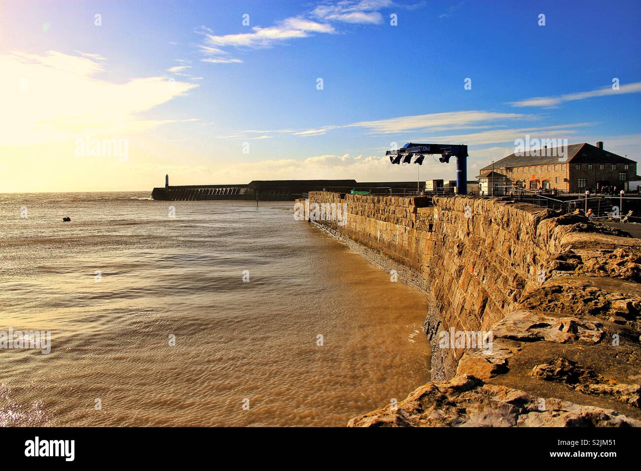 Boat lift displayed on old stone wall with lighthouse in background on a pier Stock Photo