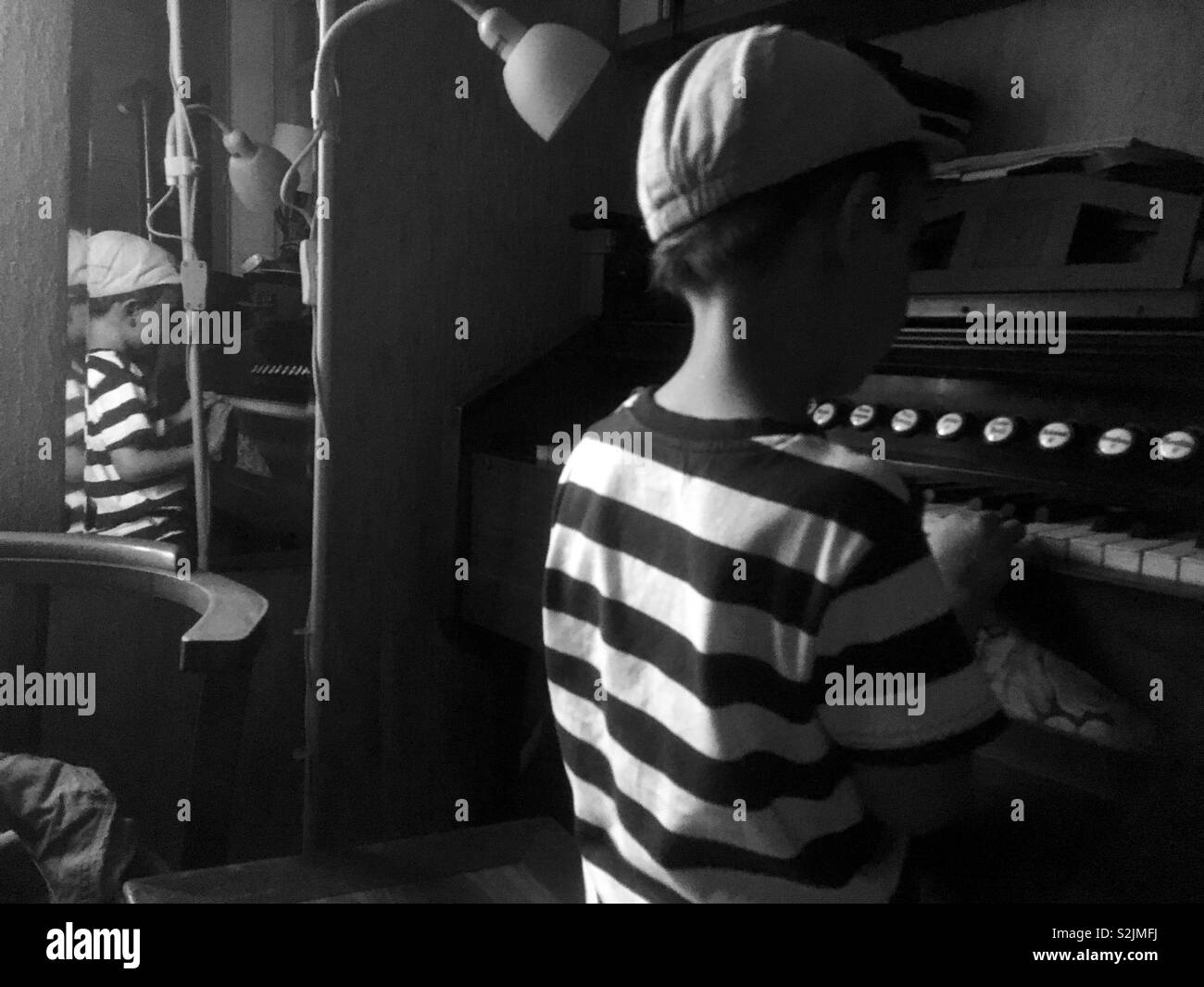 Boy child playing old harmonium in striped t-shirt, reflected in mirror, black and white image - Smartphone Captured Stock Image