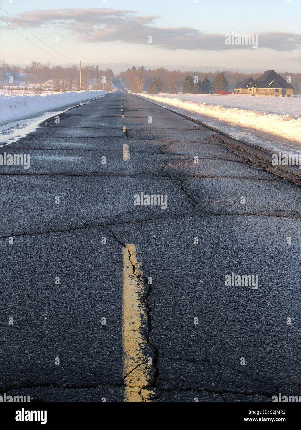 A broken yellow line on a country road in Eastern Ontario with snow on each side of the road, March 2019 - Smartphone Captured Stock Image