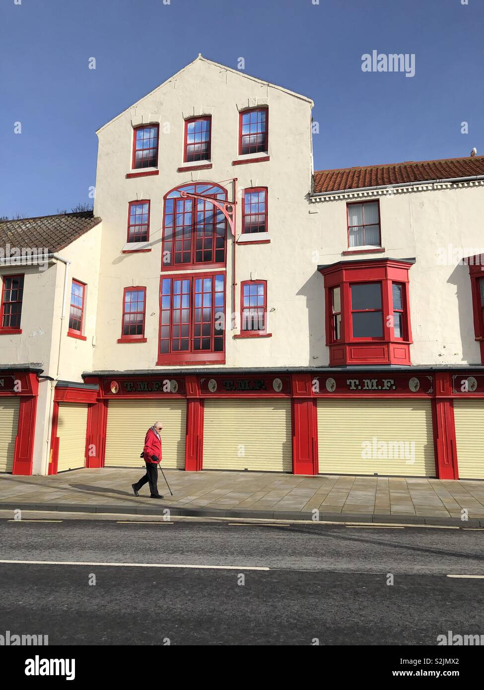 Man in red walking by a red and cream painted building - Smartphone Captured Stock Image