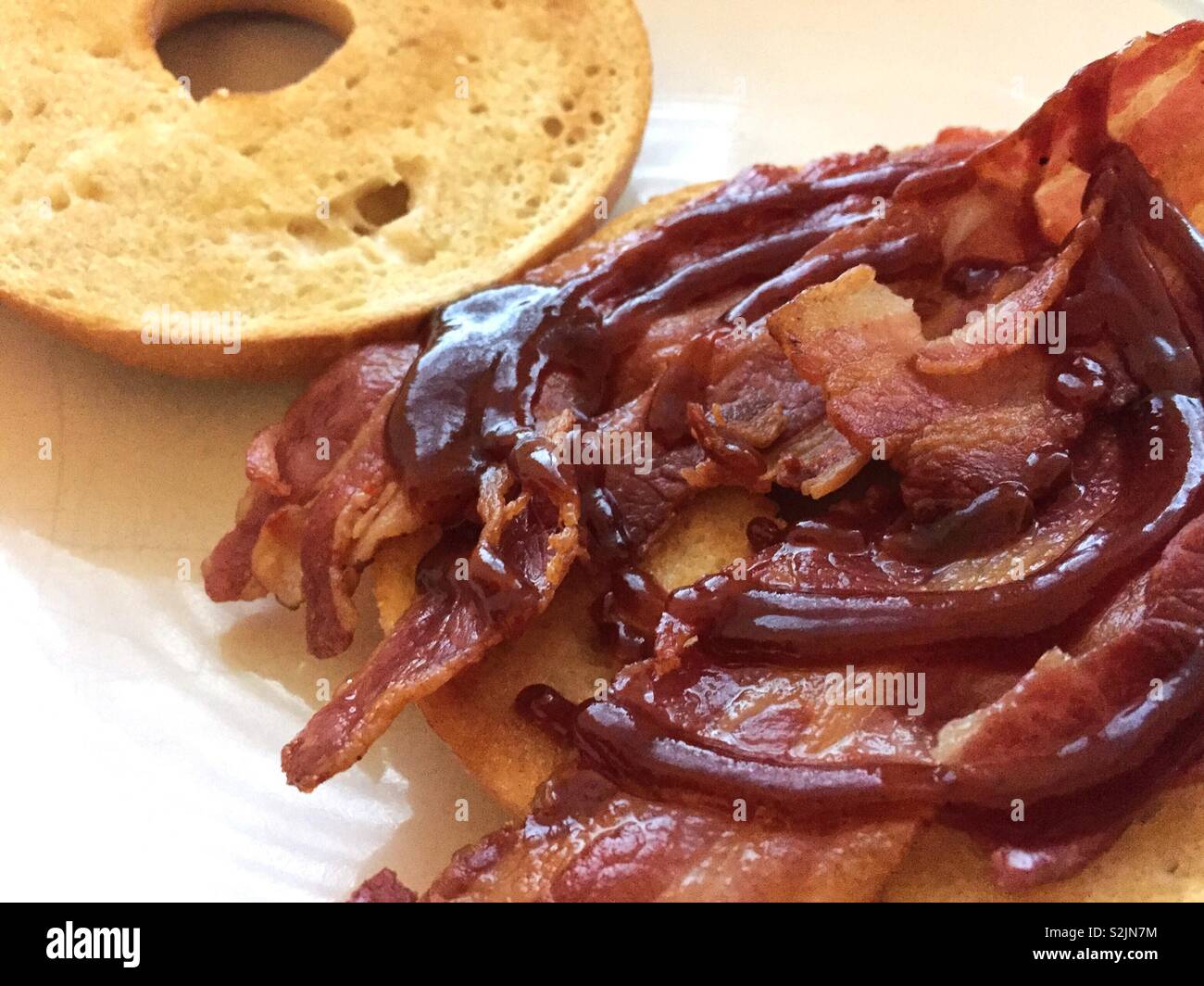 British pork free range meat.  Bacon sandwich roll.  Homemade comfort food.  Hot tasty start to the day with sauce juice tea and coffee.  Crumpet or muffin toasted and protein filled - Smartphone Captured Stock Image