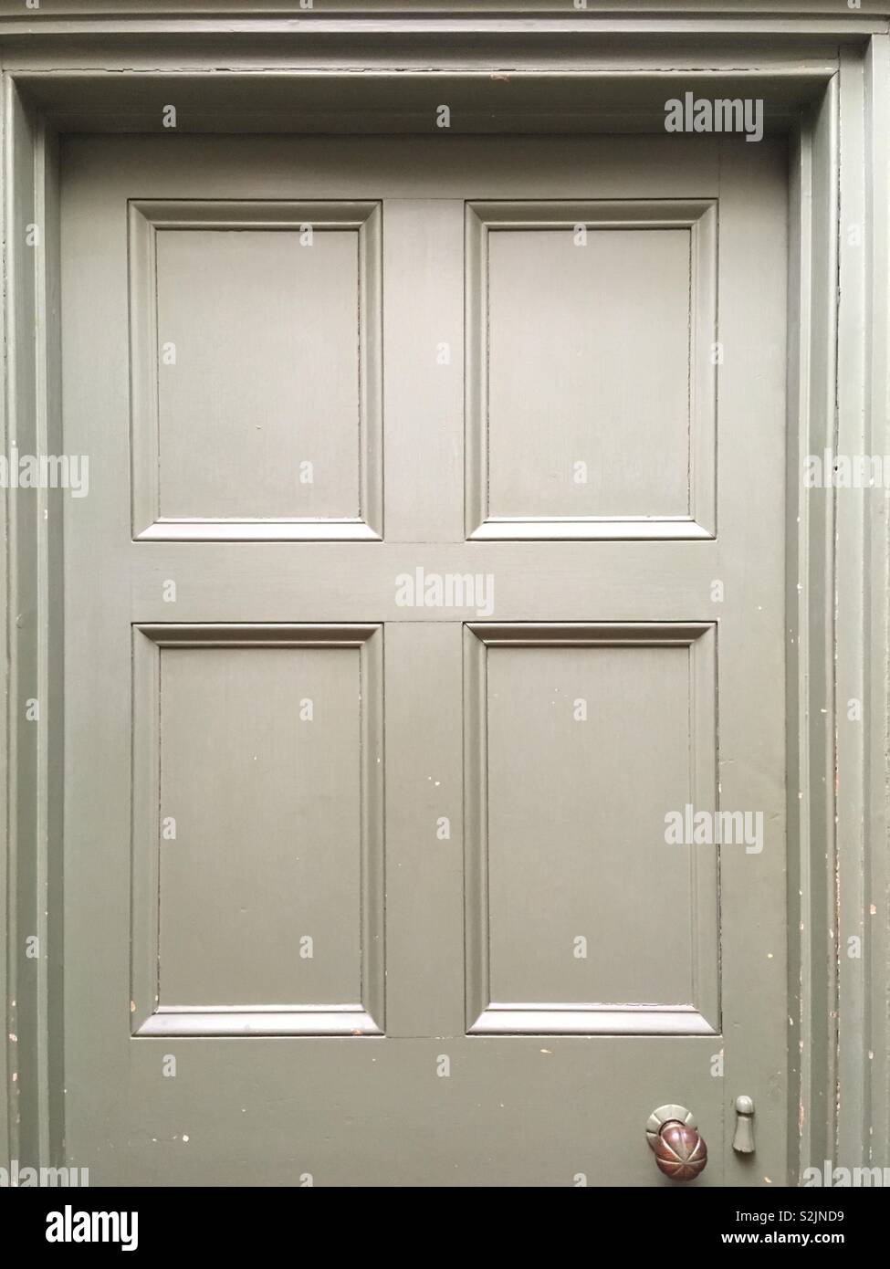 A panelled Victorian (possibly Georgian) green door, with door knob, set in a door case frame with architrave - Smartphone Captured Stock Image