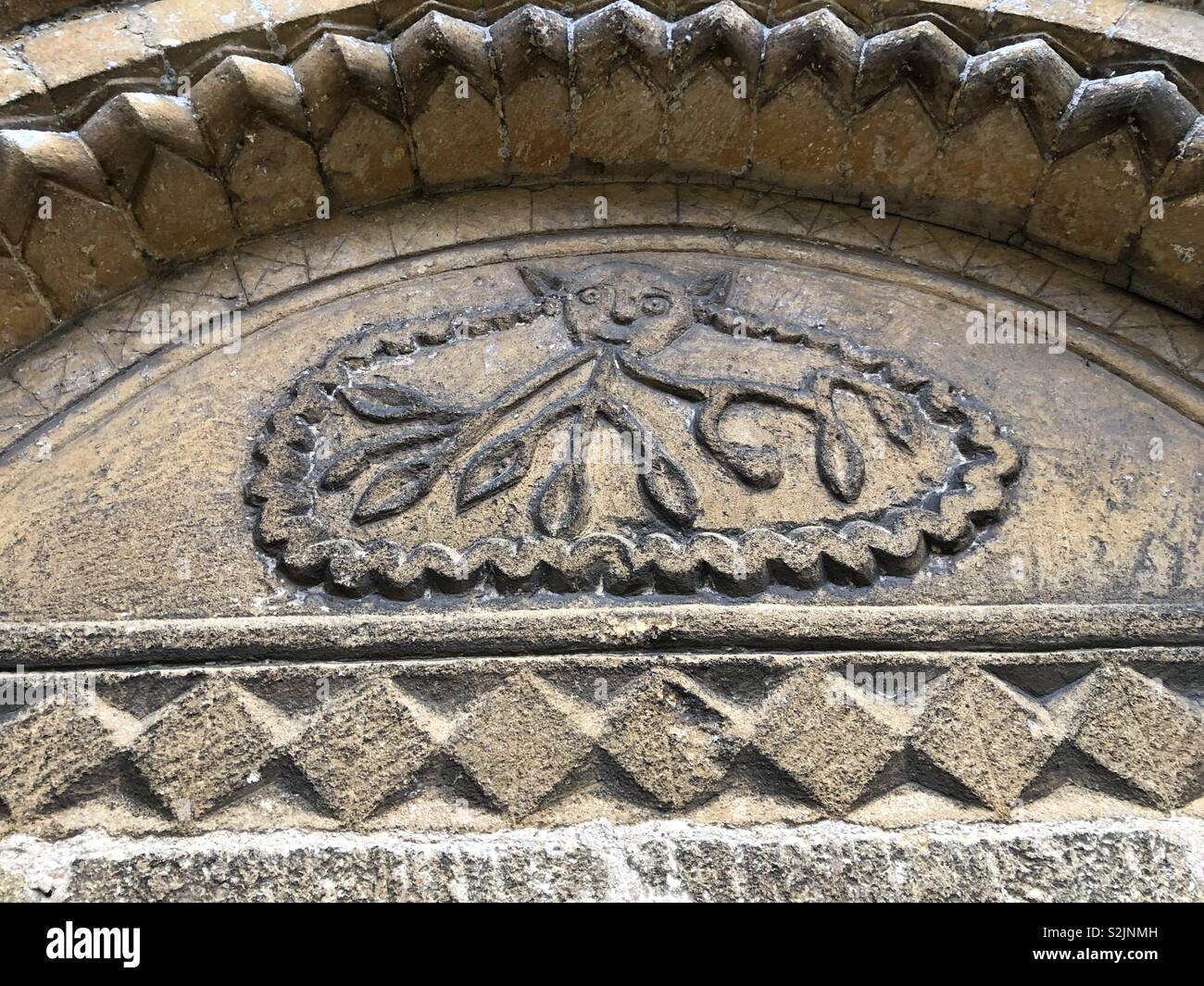 The Devil with forked tongues like snares above a church entrance in the Vale of Evesham- a warning against the lies of the Devil ensnaring the believer. - Smartphone Captured Stock Image