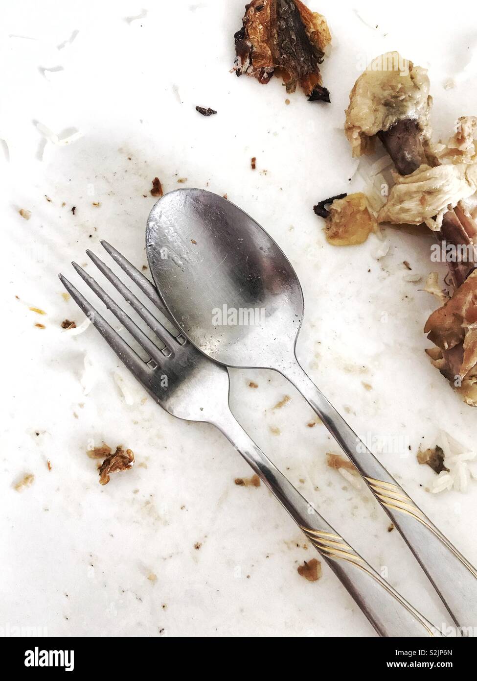 A knife and spoon with chicken bones on a plate at the end of a meal. Stock Photo