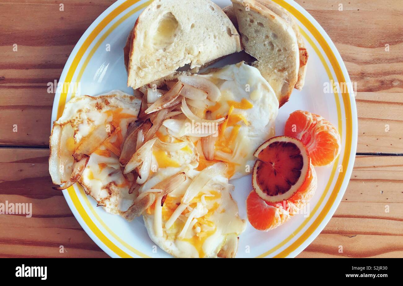 Breakfast of eggs with cheese and onion, clementines, blood orange slice, and toasted bagel Stock Photo