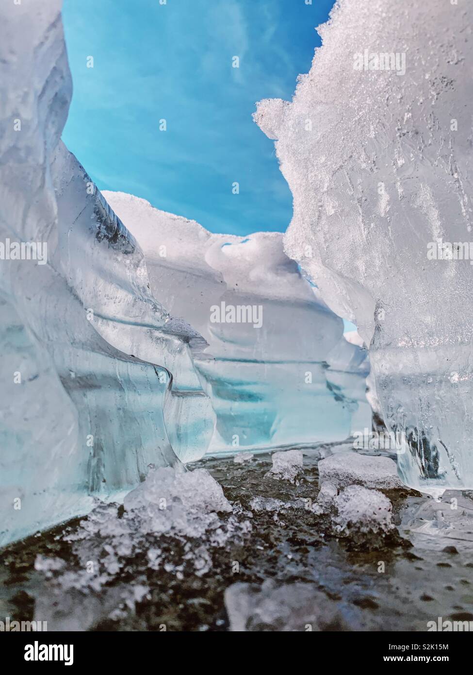 Close up of a large crack in ice surface on frozen lake as spring thaw begins with blue sky background. - Smartphone Captured Stock Image