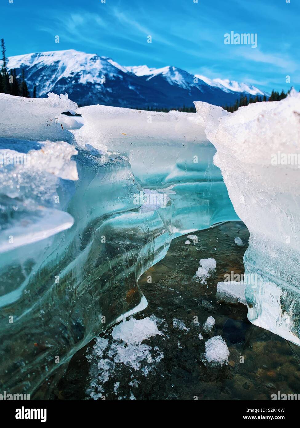 Crystal clear mountain lake ice melting on a spring sunny day with snow capped mountains in the distance in Jasper, Alberta. - Smartphone Captured Stock Image