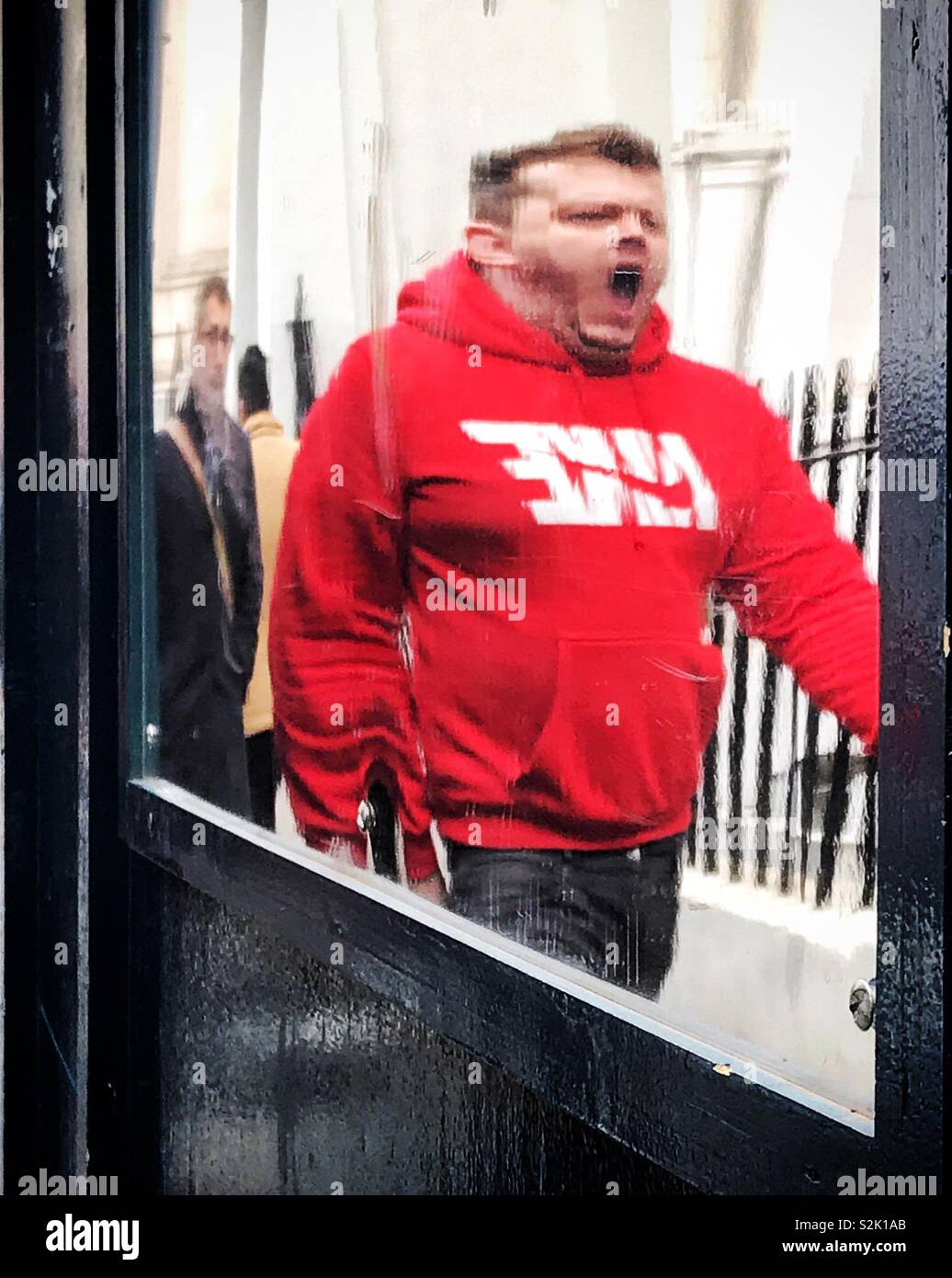 Big yawn on the way home after work. Reflection in mirror in bright red hoodie caught yawning. Distorted reflection like in amusement arcade. Stock Photo