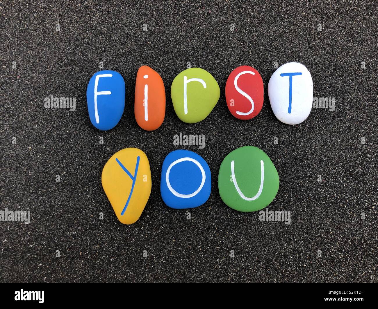 First you, motivational message composed with multi colored sea stones over natural black volcanic sand Stock Photo