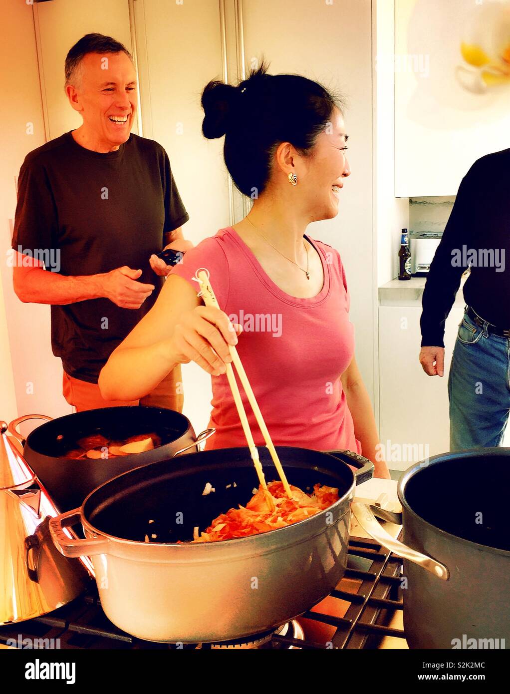 Candid spur of the moment shot of Asian woman cooking with chopsticks while entertaining in her kitchen, USA - Smartphone Captured Stock Image
