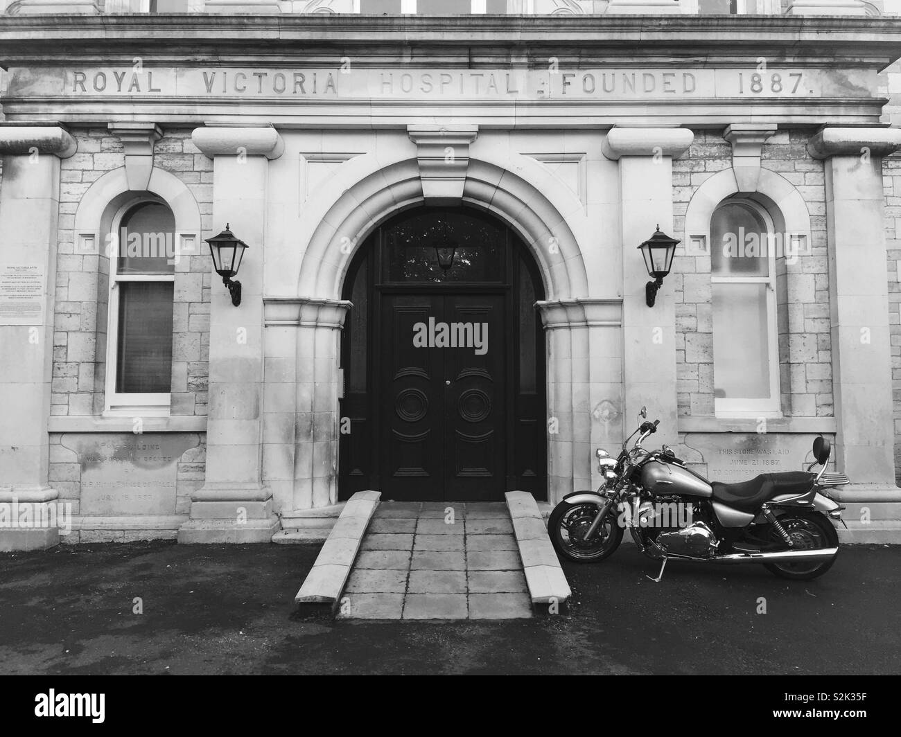 Motorcycle parked outside Victorian hospital building’s front door. Stock Photo