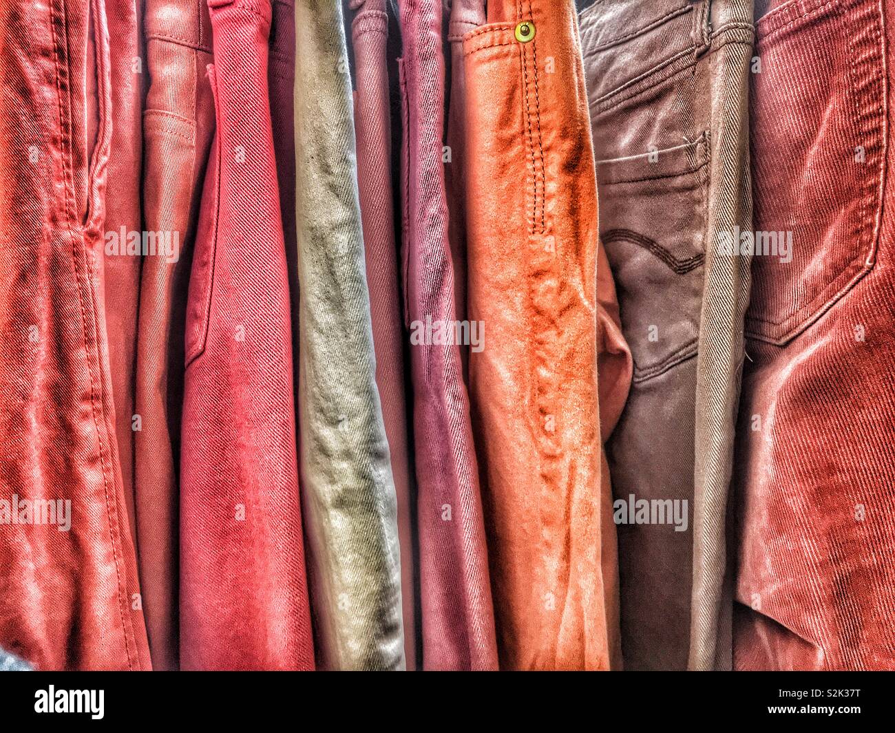 Side view of many fashionable red, brown, and orange hued jeans hanging on a clothing rack. Stock Photo