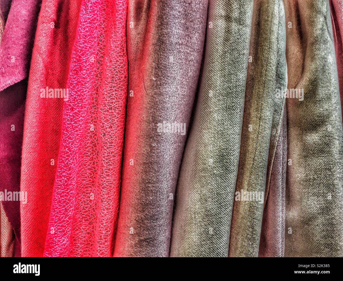 Side view of many fashionable red, purple, and black hued clothes hanging on a clothing rack. Stock Photo
