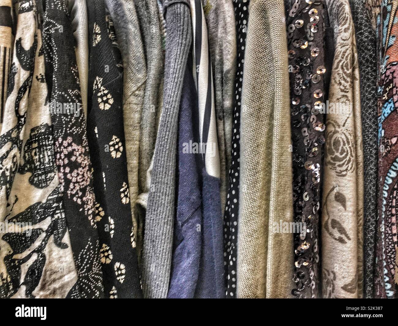 Side view of many fashionable black hued patterned blouses hanging on a clothing rack. Stock Photo