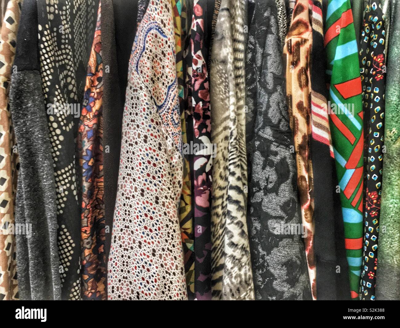 Side view of many fashionable black, green, brown, and purple hued clothes hanging on a clothing rack. Stock Photo