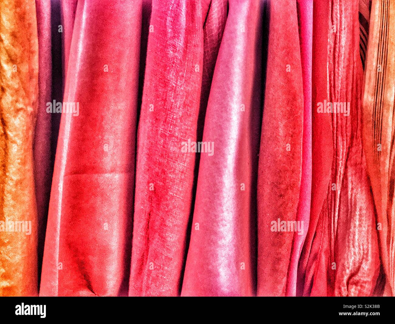 Side view of many fashionable red and gold hued clothes hanging on a clothing rack. - Smartphone Captured Stock Image