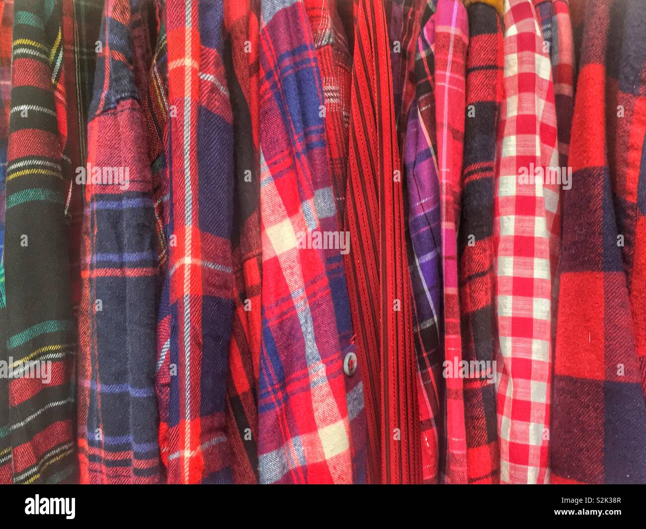 Side view of many fashionable red, blue, and black hued patterned and checkered clothes hanging on a clothing rack. Stock Photo